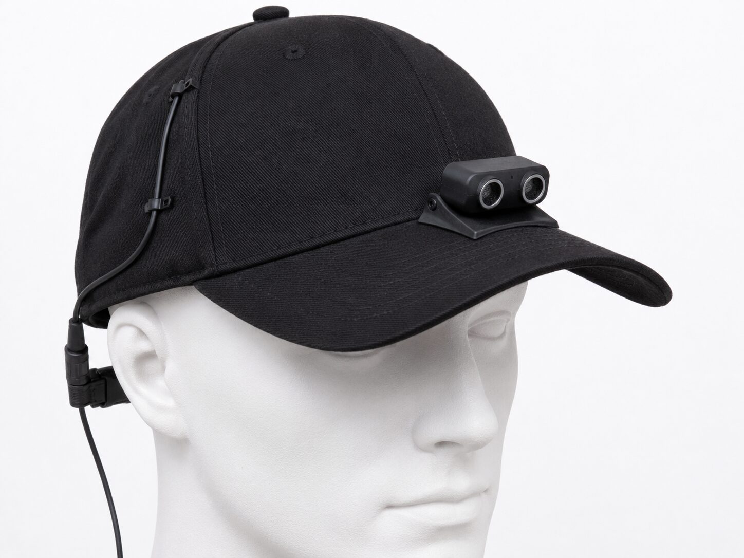 Concept mockup: black baseball cap on a mannequin head with a small ultrasonic distance sensor mounted on the brim, a thin cable routed along the cap seam.